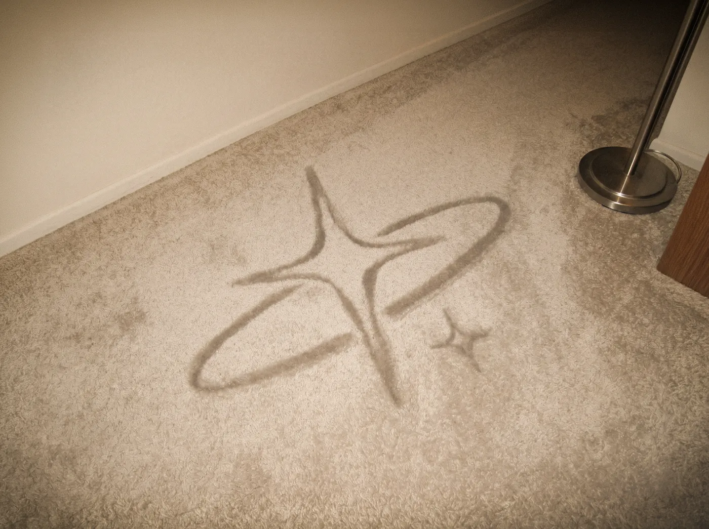 The star-and-orbit sigil pressed and worn into the pile of a beige domestic carpet.